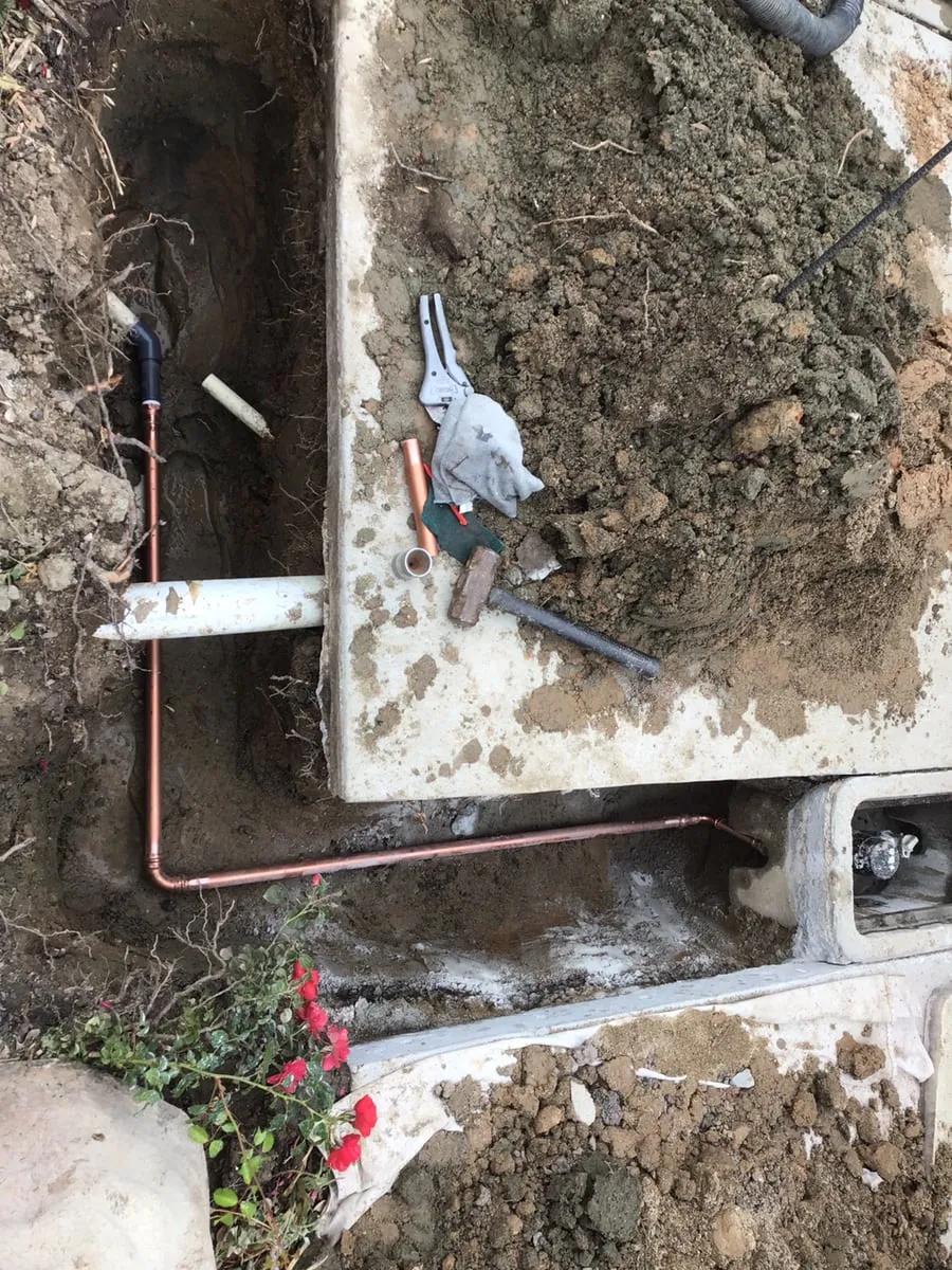 A new copper water line laid in a trench beside a concrete slab, running to the meter box