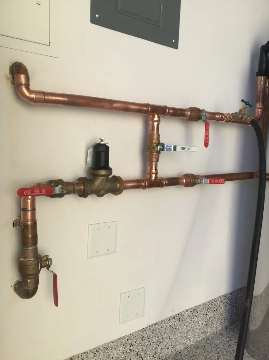 Copper water piping with a pressure regulator and shut-off valves on a garage wall
