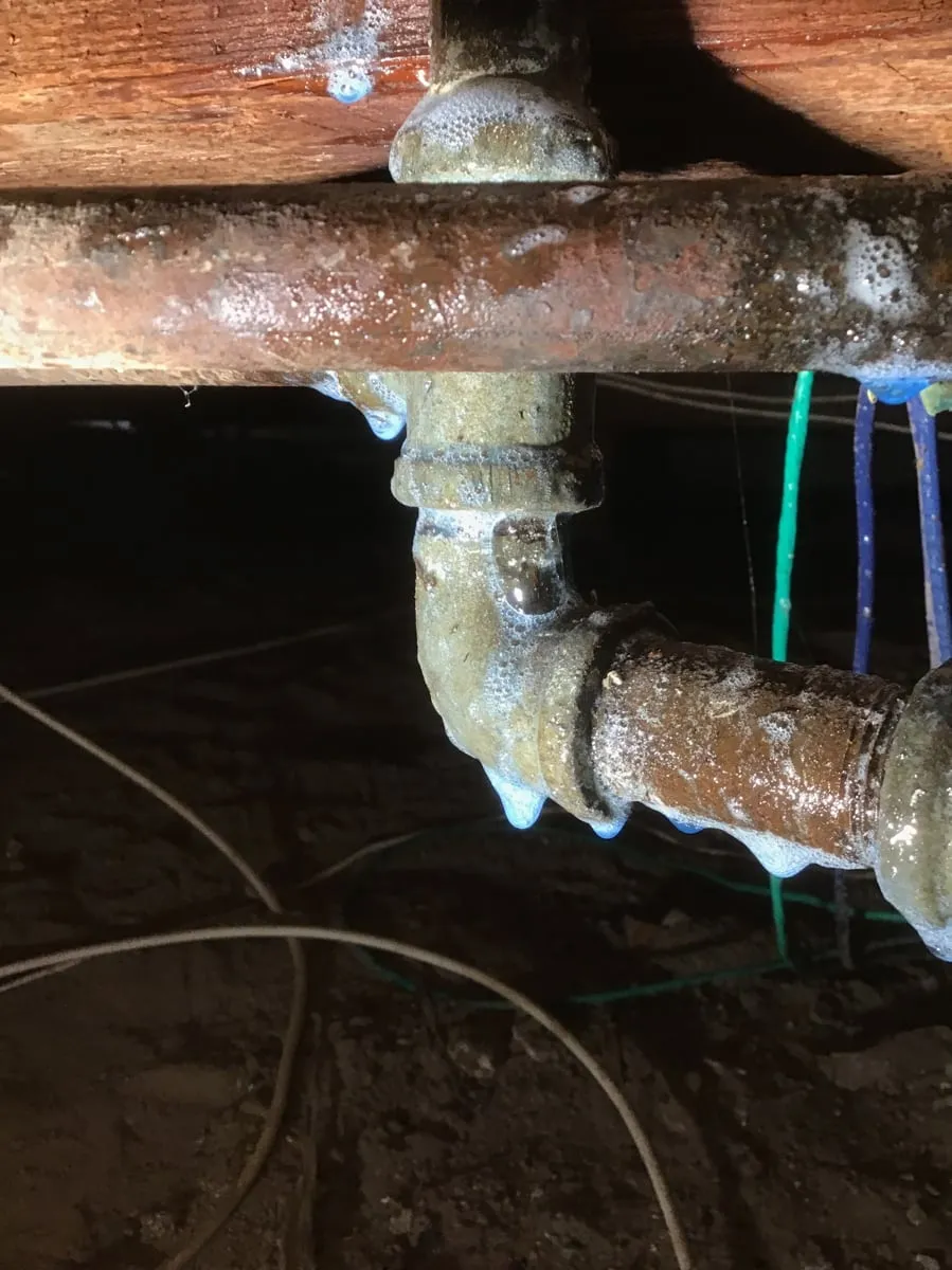 Corroded galvanized pipe and fittings under a house, seen from the crawl space