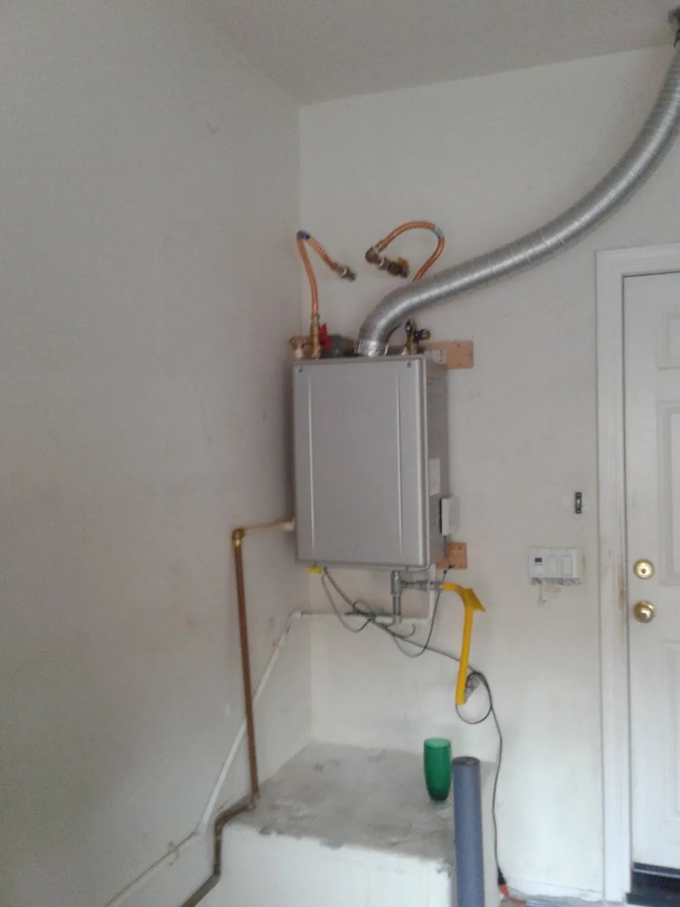 A tankless water heater installed on a garage wall, with its vent and copper water lines