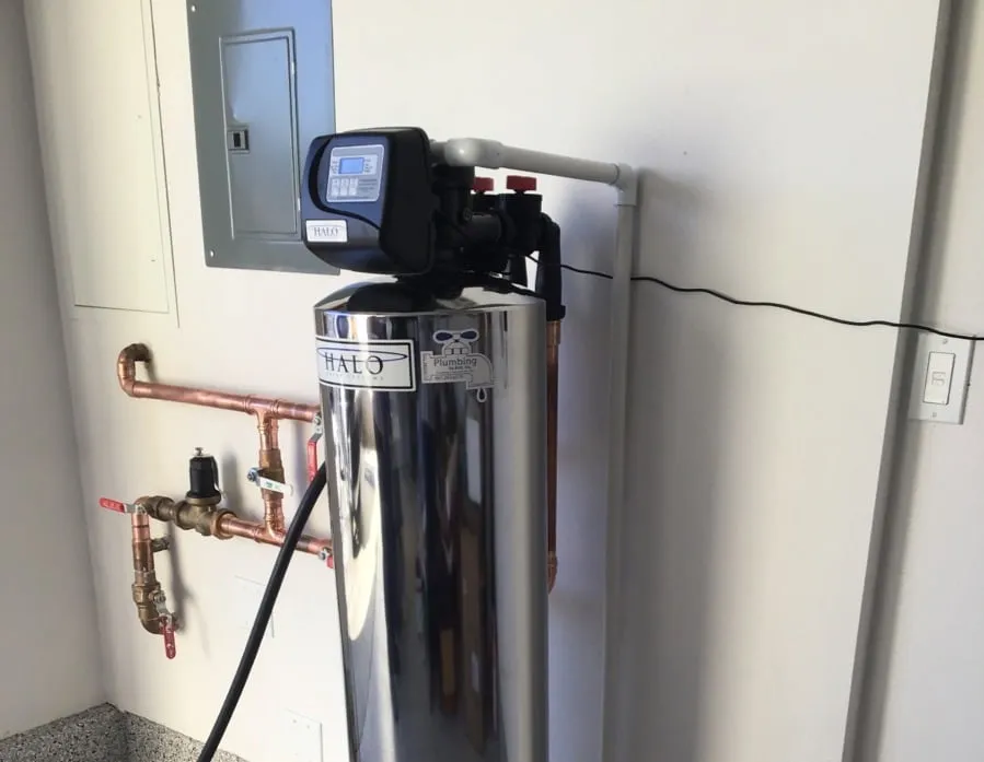 A whole-house water treatment tank installed on a garage wall beside the electrical panel
